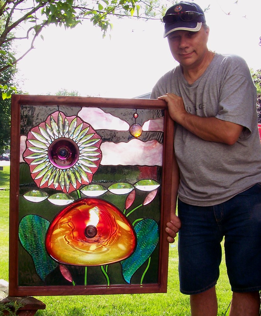 An artist holds up one of his windows for show. 